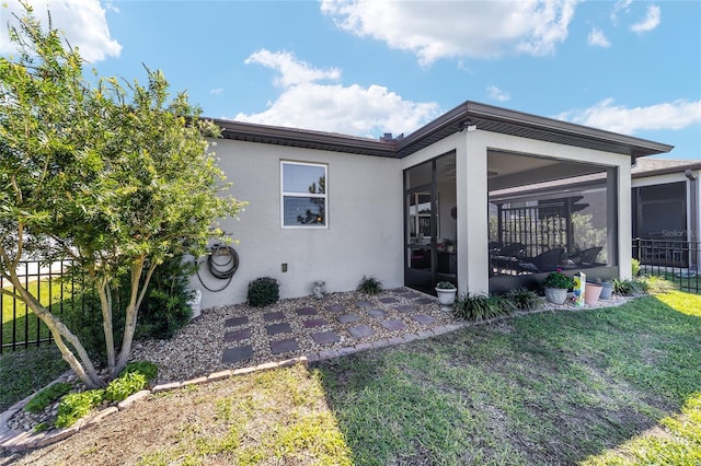 exterior space with fence, stucco siding, a lawn, a sunroom, and a patio