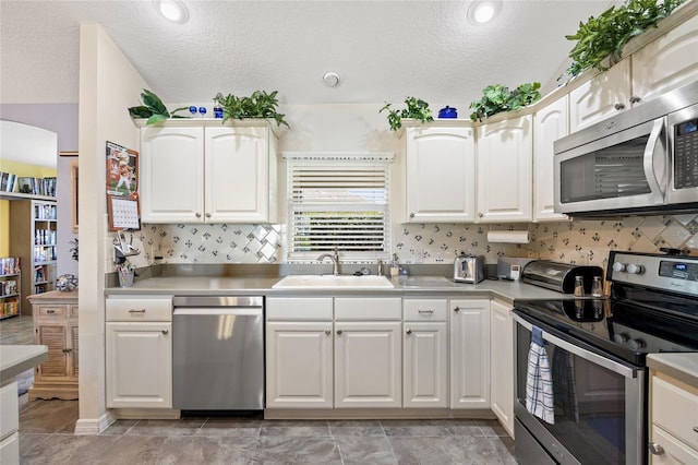 kitchen with light countertops, decorative backsplash, stainless steel appliances, white cabinetry, and a sink