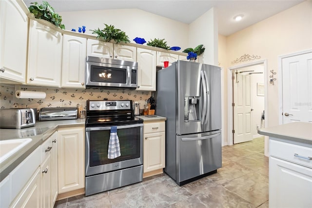 kitchen with backsplash, appliances with stainless steel finishes, light countertops, and lofted ceiling