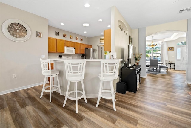 kitchen with white microwave, light wood-style flooring, arched walkways, freestanding refrigerator, and brown cabinets