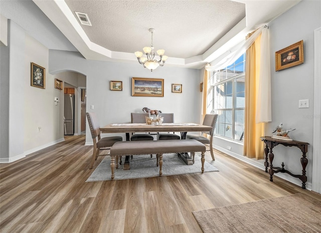 dining room with light wood-type flooring, a raised ceiling, arched walkways, and a textured ceiling