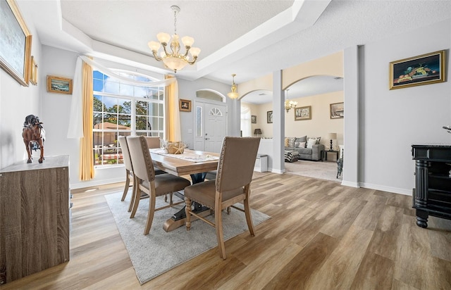 dining room with a notable chandelier, a tray ceiling, arched walkways, light wood-style floors, and baseboards