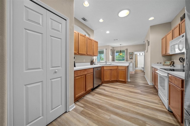 kitchen featuring light countertops, light wood-style flooring, a peninsula, white appliances, and a sink