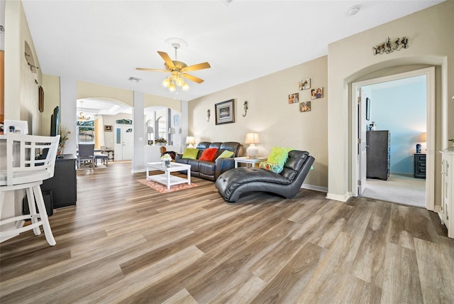 living room with ceiling fan, baseboards, arched walkways, and wood finished floors