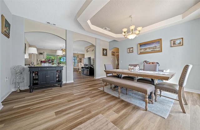 dining area with light wood-type flooring, a tray ceiling, arched walkways, and visible vents