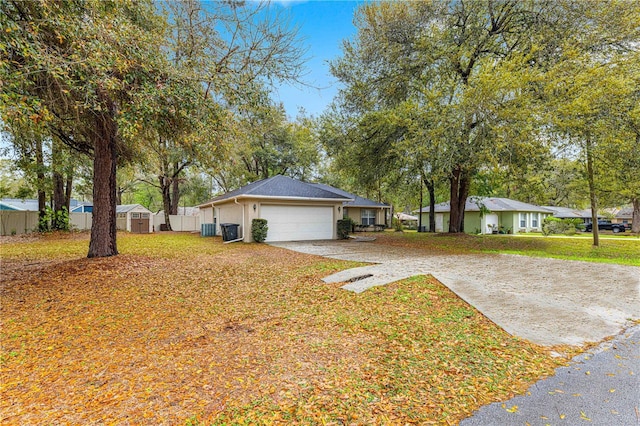 view of front facade featuring a front lawn, fence, concrete driveway, central AC unit, and a garage