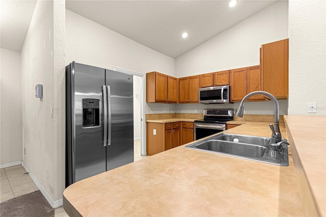 kitchen with brown cabinets, a sink, appliances with stainless steel finishes, light tile patterned flooring, and light countertops