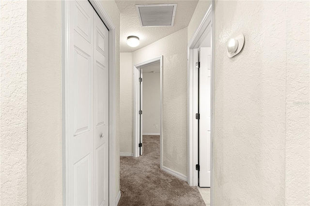 hall featuring visible vents, carpet floors, a textured ceiling, and a textured wall