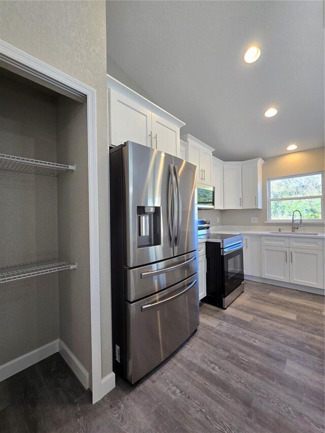 kitchen with a sink, stainless steel appliances, dark wood-type flooring, light countertops, and white cabinetry