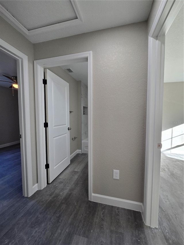 hallway featuring visible vents, wood finished floors, baseboards, and a textured wall