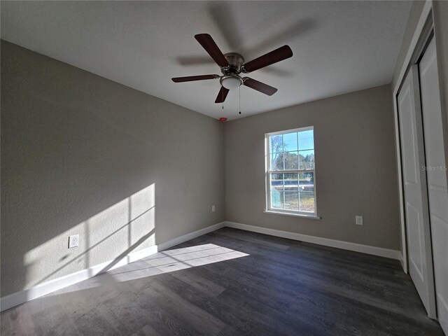 unfurnished bedroom featuring a closet, baseboards, ceiling fan, and dark wood-style flooring