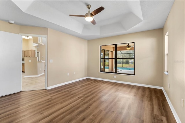 spare room featuring ceiling fan with notable chandelier, a raised ceiling, baseboards, and wood finished floors