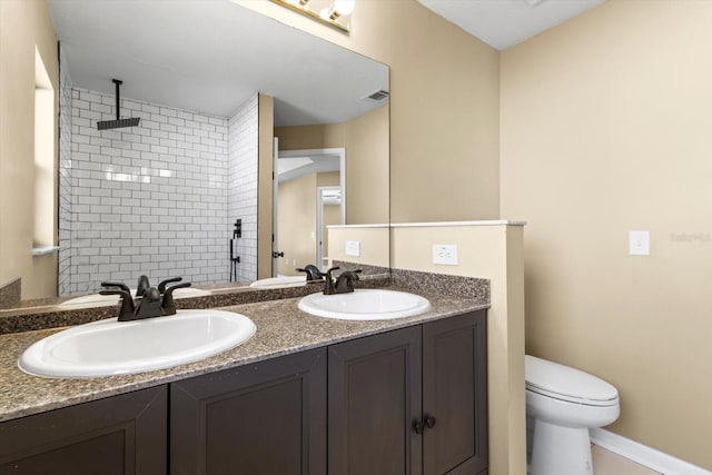 full bathroom with double vanity, toilet, tiled shower, and a sink