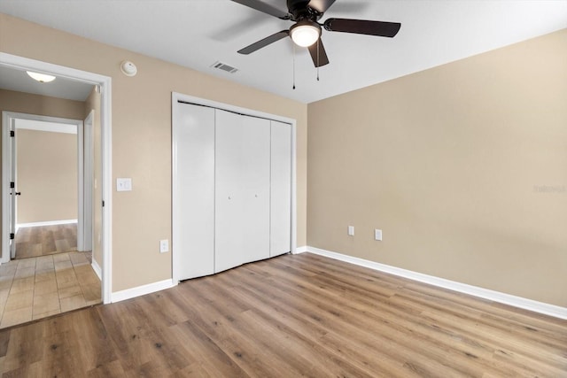 unfurnished bedroom with a ceiling fan, wood finished floors, visible vents, baseboards, and a closet