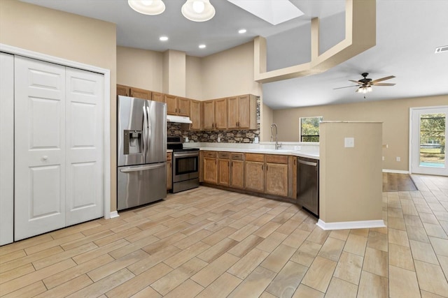 kitchen with a sink, light countertops, under cabinet range hood, appliances with stainless steel finishes, and backsplash