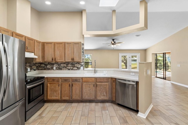 kitchen with under cabinet range hood, light countertops, decorative backsplash, appliances with stainless steel finishes, and a sink