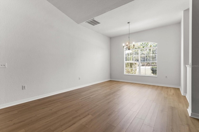 unfurnished room with visible vents, baseboards, an inviting chandelier, and wood finished floors