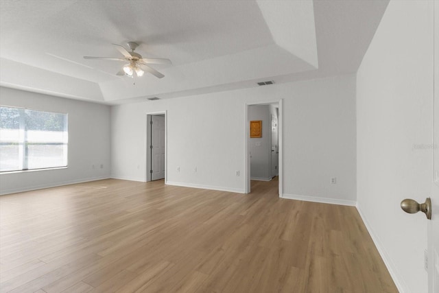 unfurnished room with visible vents, ceiling fan, baseboards, a tray ceiling, and light wood-style floors