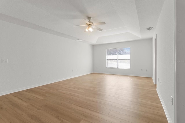 empty room with baseboards, visible vents, a tray ceiling, ceiling fan, and light wood-style floors