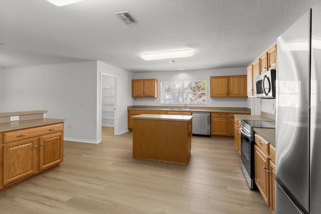 kitchen featuring appliances with stainless steel finishes, a kitchen island, light wood-style floors, and a sink