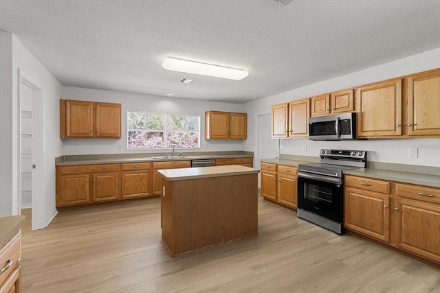 kitchen featuring a center island, light wood-type flooring, brown cabinetry, stainless steel appliances, and a sink