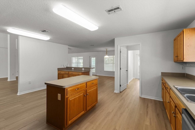 kitchen with visible vents, a sink, a kitchen island, brown cabinetry, and dishwasher