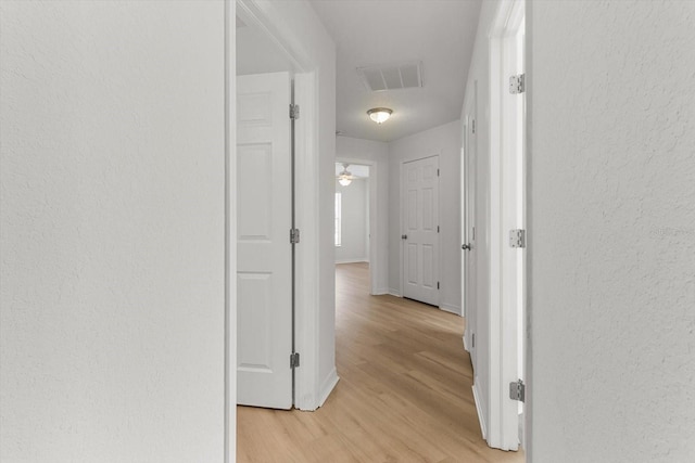 corridor with a textured wall, visible vents, light wood finished floors, and baseboards