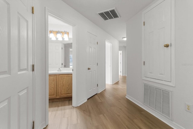 hallway with a sink, visible vents, baseboards, and light wood-style floors