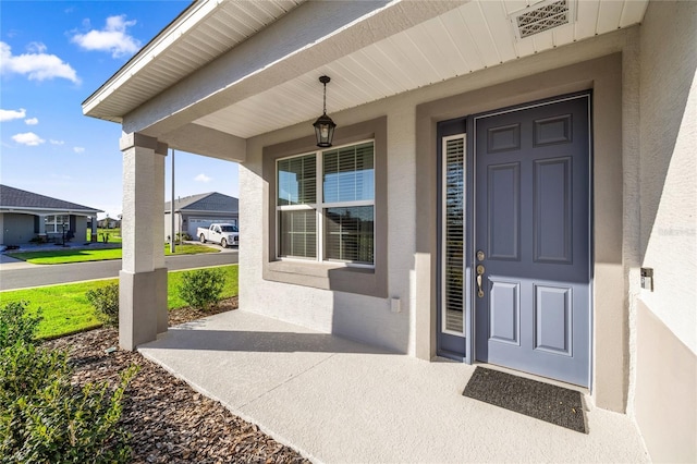 doorway to property featuring visible vents, stucco siding, and a porch