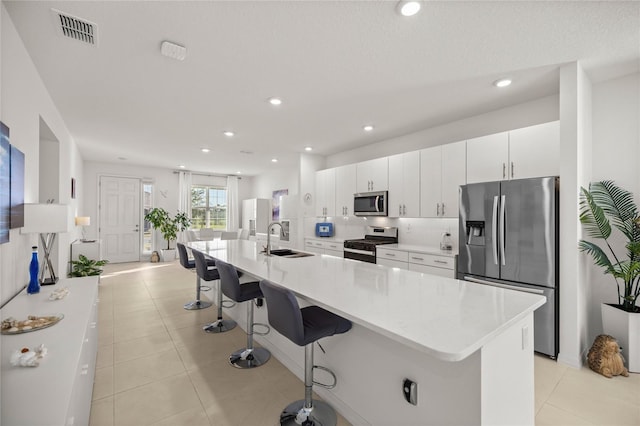 kitchen featuring visible vents, a kitchen bar, a sink, white cabinetry, and appliances with stainless steel finishes