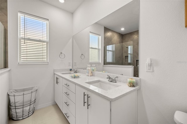 bathroom with tile patterned flooring, baseboards, double vanity, a tile shower, and a sink