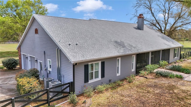 rear view of property featuring cooling unit, fence, roof with shingles, a chimney, and a garage