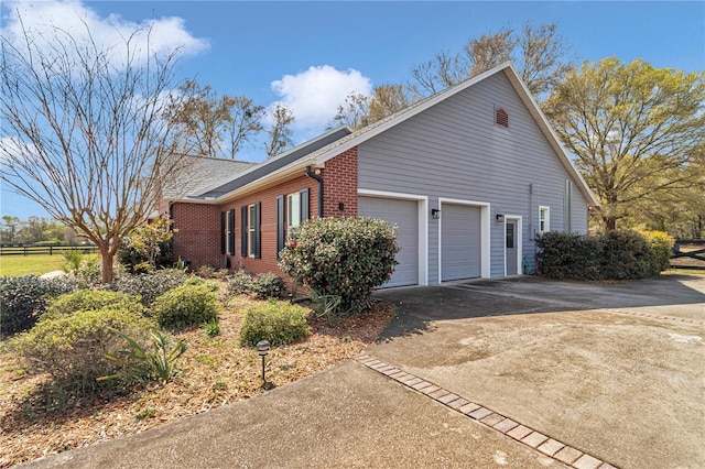 view of home's exterior featuring brick siding, an attached garage, driveway, and fence