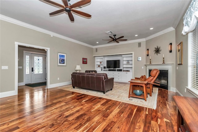 living area featuring a glass covered fireplace, baseboards, wood finished floors, and ornamental molding