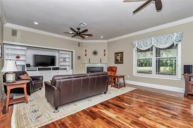 living room featuring wood finished floors, crown molding, a fireplace, and visible vents