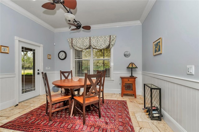 dining space featuring crown molding, stone tile floors, a wainscoted wall, and ceiling fan