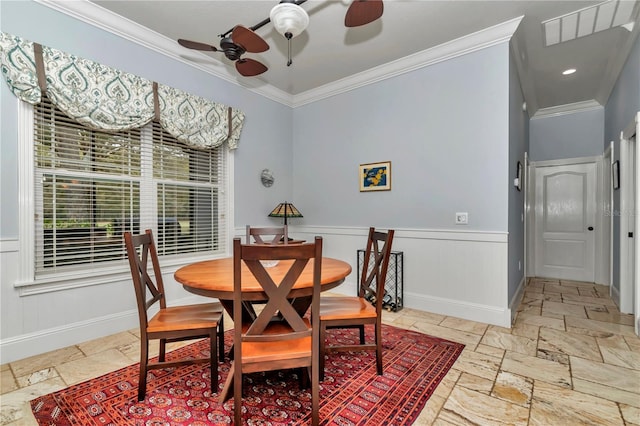 dining area with baseboards, ceiling fan, a wainscoted wall, ornamental molding, and stone tile floors