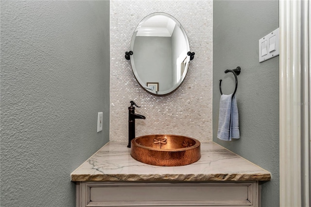 bathroom featuring tasteful backsplash, ornamental molding, vanity, and a textured wall