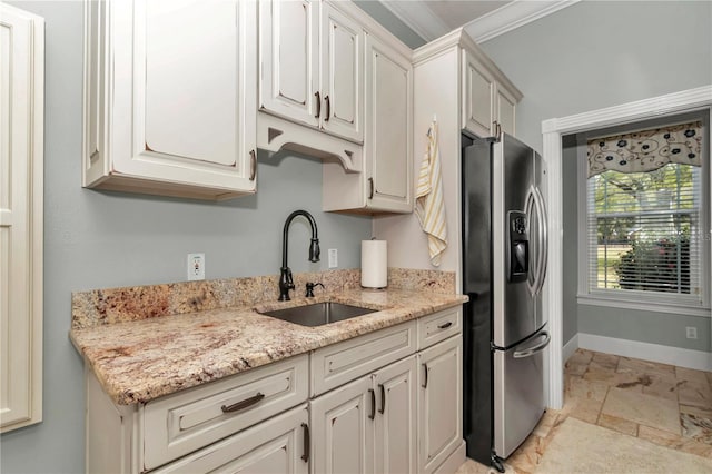 kitchen featuring ornamental molding, a sink, stone tile flooring, stainless steel fridge, and baseboards