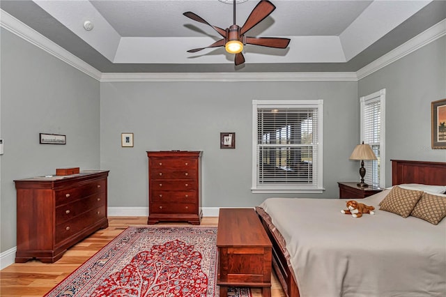 bedroom with baseboards, a raised ceiling, light wood-style flooring, and crown molding