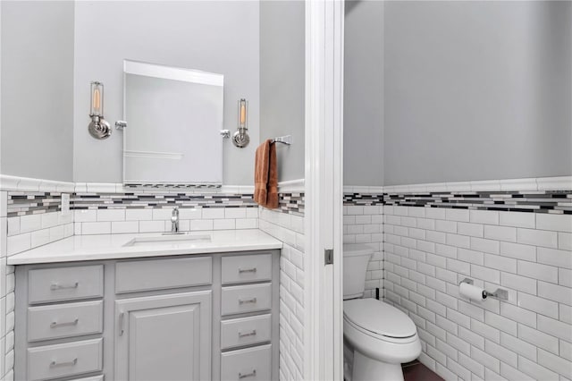 bathroom with toilet, tile walls, wainscoting, and vanity