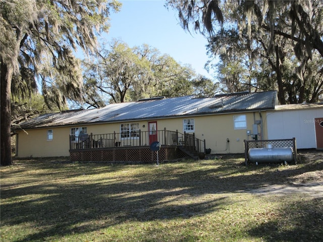 rear view of property featuring a yard, metal roof, heating fuel, and a deck