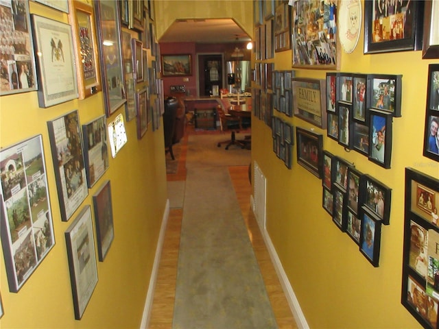 corridor featuring wood finished floors, baseboards, and arched walkways