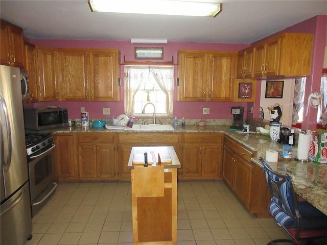 kitchen with a sink, stainless steel appliances, brown cabinetry, and light tile patterned floors