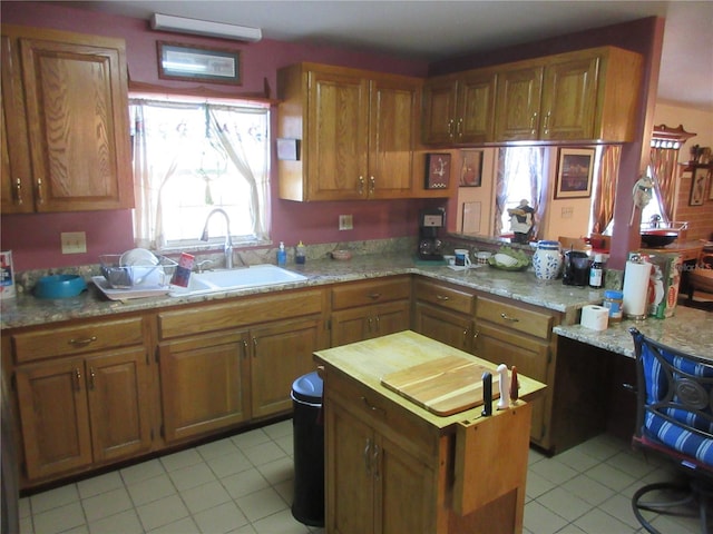 kitchen with light stone counters, light tile patterned floors, brown cabinetry, and a sink