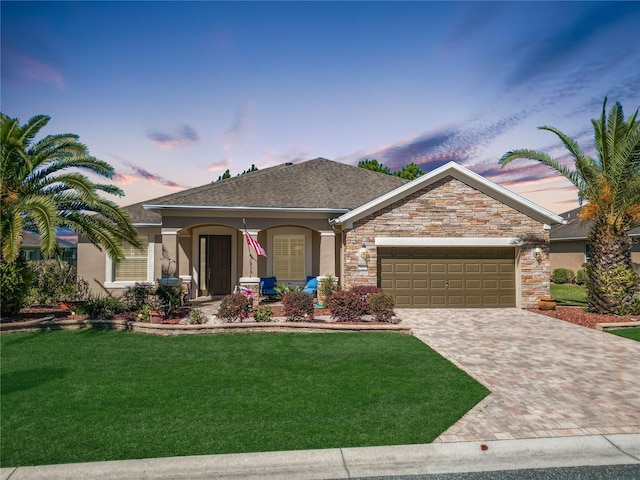 ranch-style house featuring stucco siding, an attached garage, a lawn, and decorative driveway