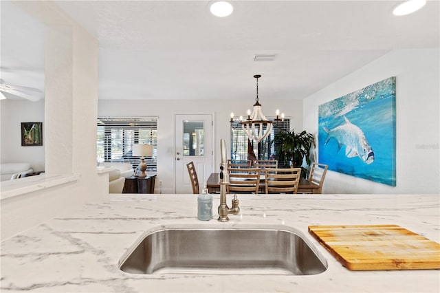 kitchen featuring visible vents, ceiling fan with notable chandelier, a sink, light stone countertops, and hanging light fixtures