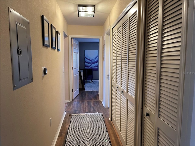 hallway featuring electric panel, baseboards, dark wood-style flooring, and a textured wall