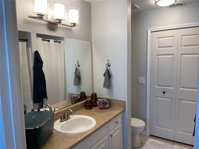 bathroom with visible vents, toilet, vanity, and a textured wall