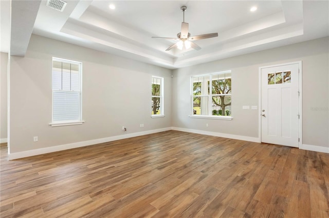 empty room featuring visible vents, baseboards, a tray ceiling, and wood finished floors